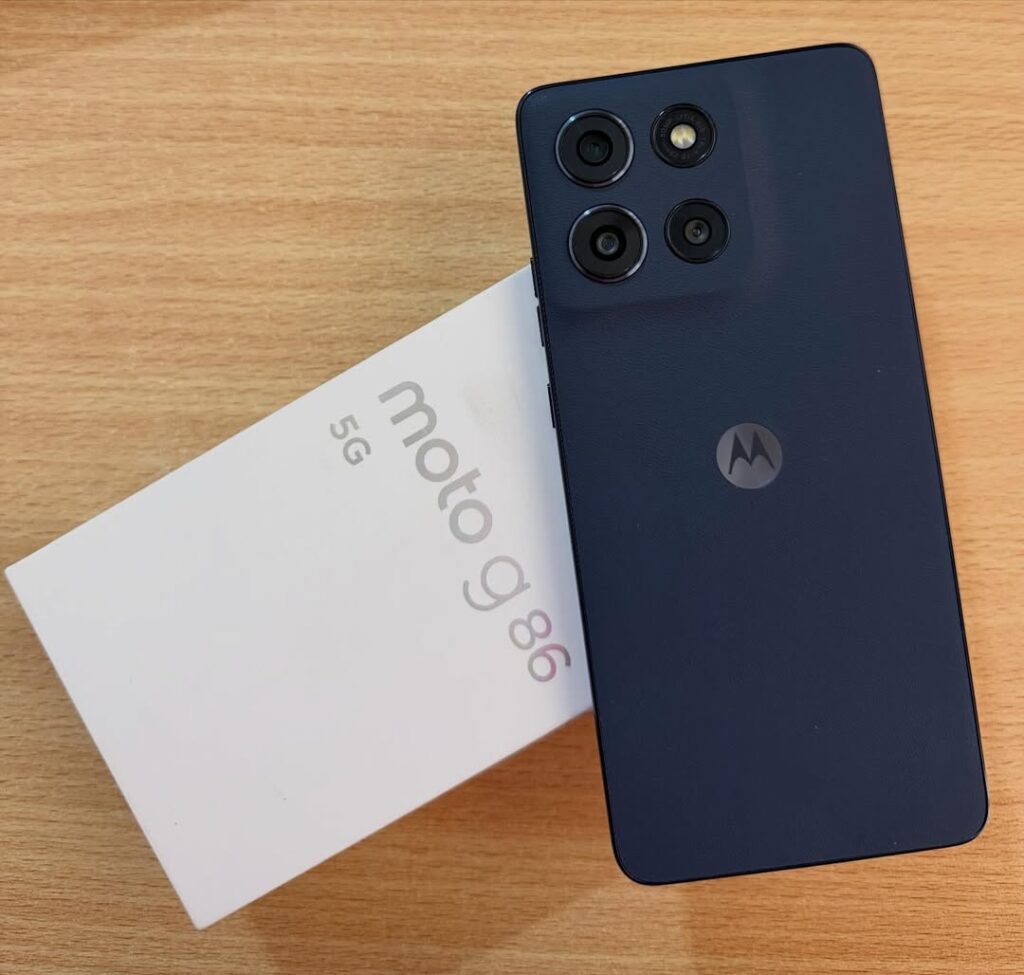 Moto G86 5G azul-marinho apoiado sobre a caixa original em cenário de mesa de madeira com iluminação ambiente.